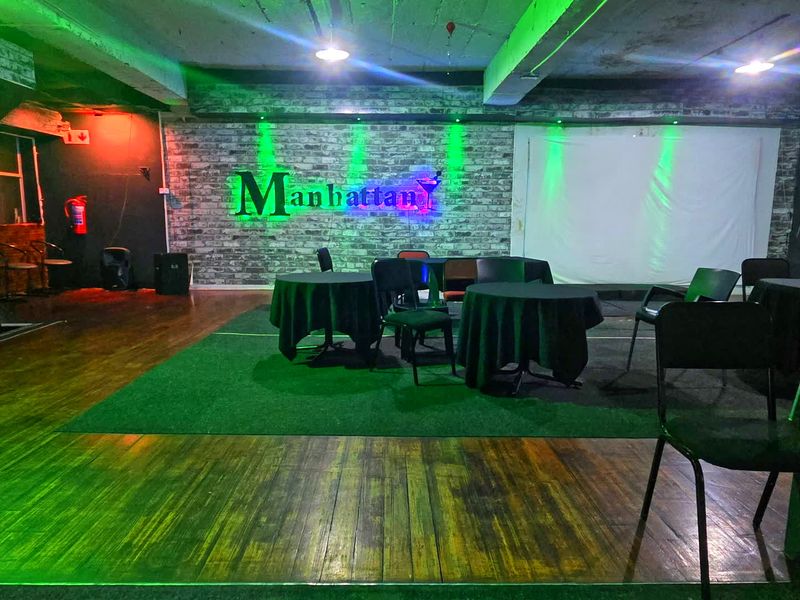 Commercial clubhouse space featuring exposed concrete ceilings, brick accent wall, and hardwood flooring, currently set up for event use.