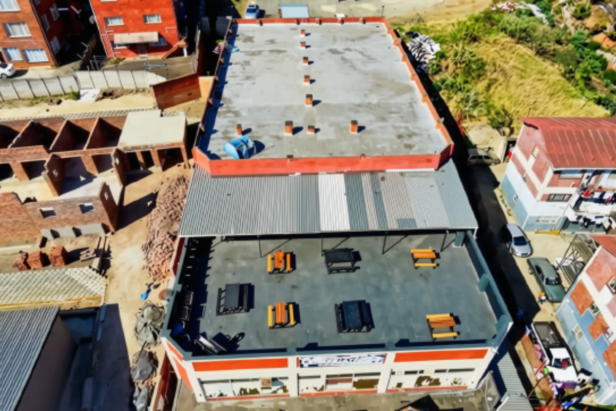 Aerial view of a commercial building featuring a flat roof, a covered outdoor terrace area, and surrounding urban development.