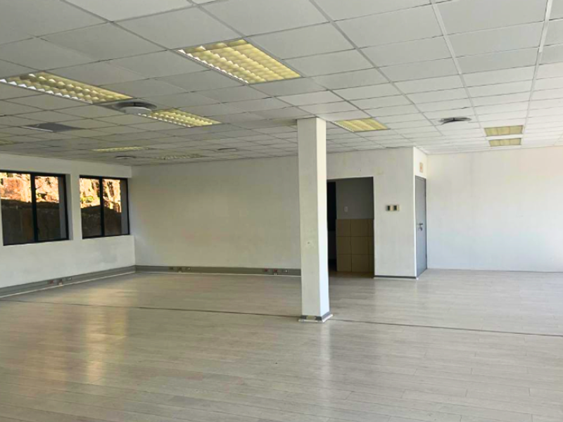 An open-plan office space featuring a suspended ceiling with recessed lighting, laminate flooring, and a central structural column.