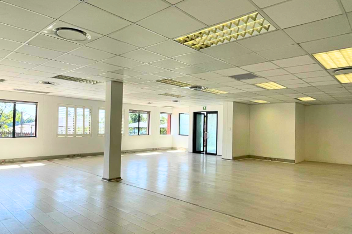 Spacious, open-plan office area featuring a suspended ceiling with recessed lighting, laminate flooring, and large windows providing ample natural light.