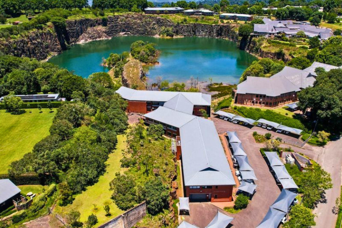 Aerial view of a professional office complex featuring extensive landscaped grounds, ample shaded parking, and scenic views overlooking a large quarry lake.