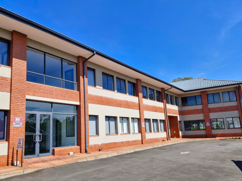 A professional exterior view of a modern office building featuring a brick and render facade, large windows, and a paved driveway entrance.