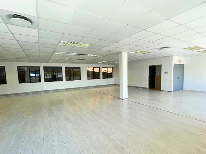 A spacious, open-plan office area featuring a suspended ceiling, recessed lighting, and large windows providing ample natural light.
