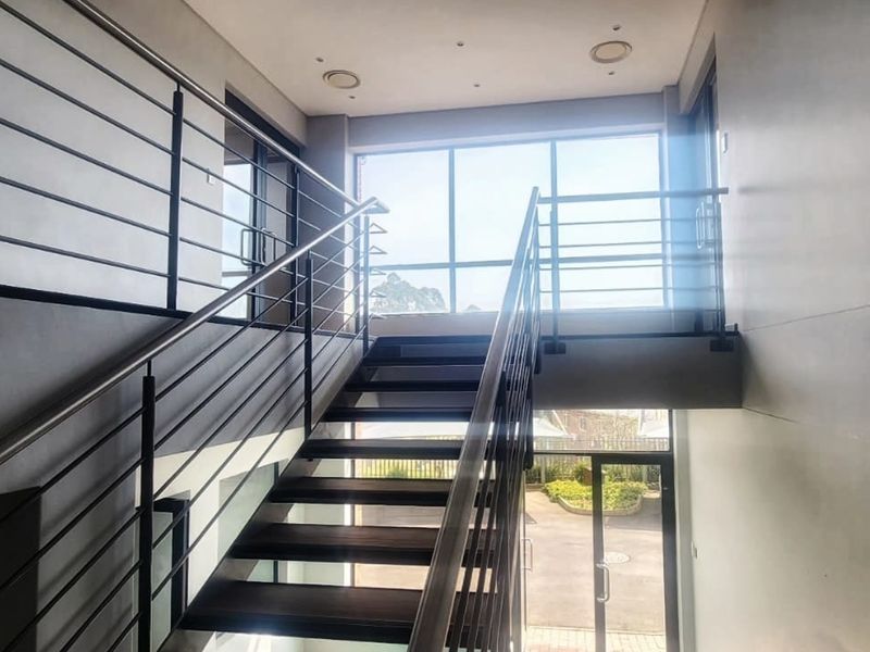 Modern office building entrance featuring a contemporary staircase with stainless steel balustrades and large windows providing ample natural light.