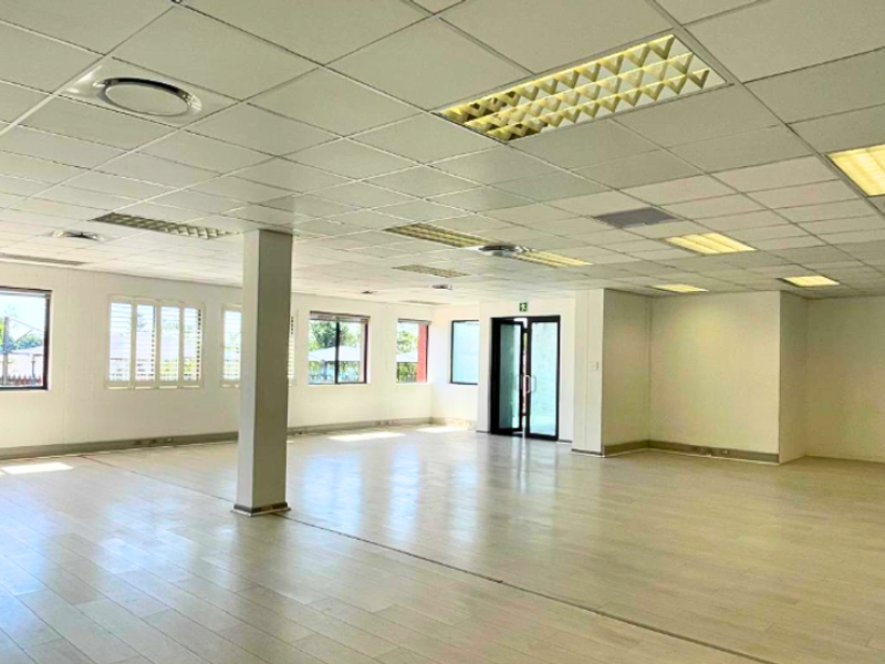Spacious, open-plan office area featuring a suspended ceiling with recessed lighting, laminate flooring, and large windows providing ample natural light.