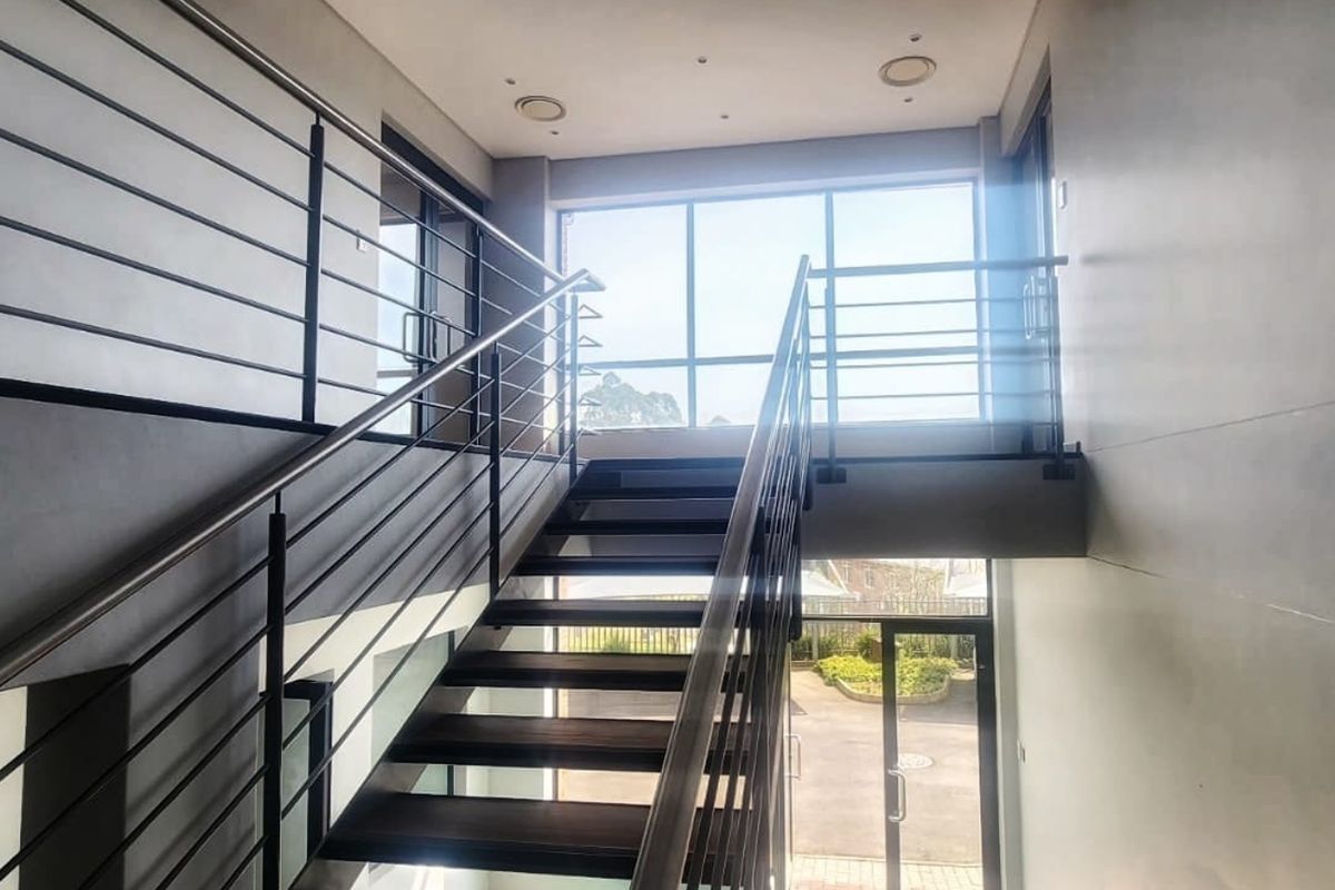 Modern office building entrance featuring a contemporary staircase with stainless steel balustrades and large windows providing ample natural light.