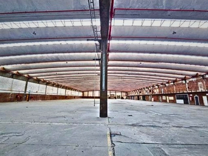 Expansive industrial warehouse space featuring high vaulted ceilings with exposed steel trusses, concrete flooring, and integrated fire sprinkler systems.