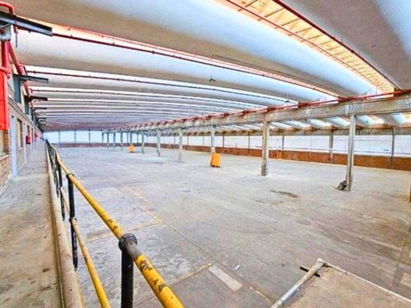 Expansive industrial warehouse space featuring high ceilings with exposed ventilation, concrete flooring, and robust steel structural elements.