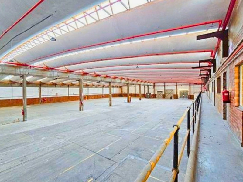 Expansive industrial warehouse space featuring high ceilings with exposed fire sprinkler systems, concrete flooring, and robust steel structural supports.