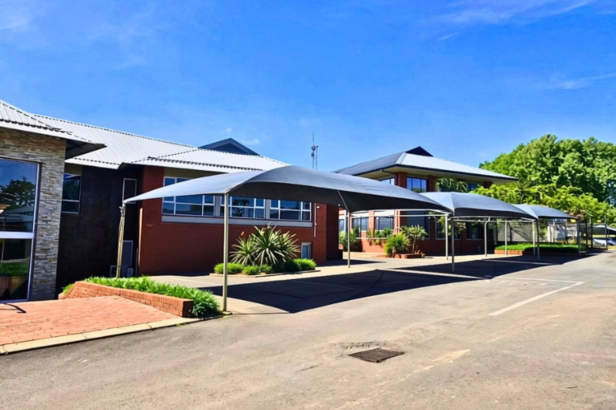 Exterior view of a professional office building featuring a brick facade, stone accents, and covered parking bays with shade sails.