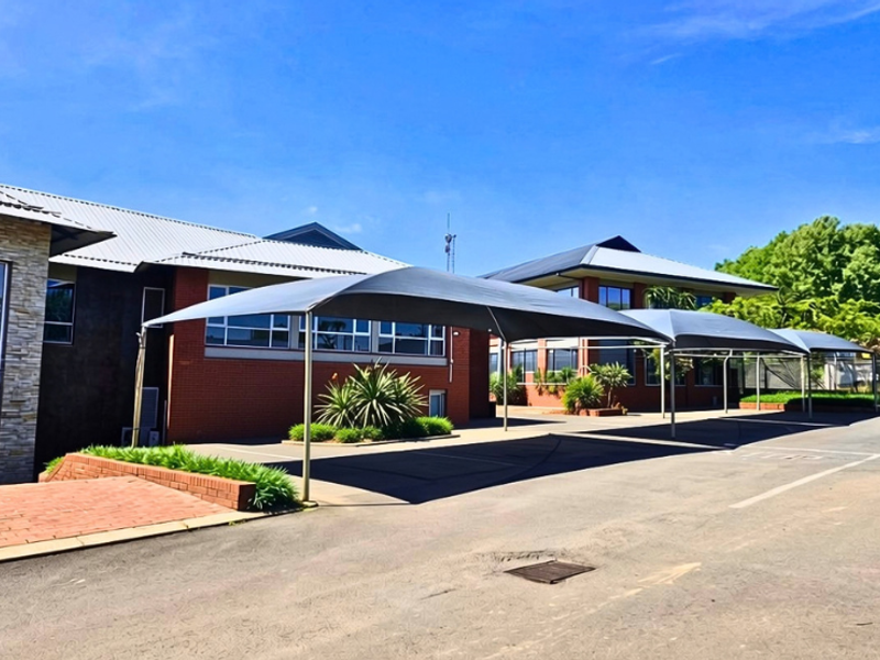 Exterior view of a professional office building featuring a brick facade, stone accents, and covered parking bays with shade sails.