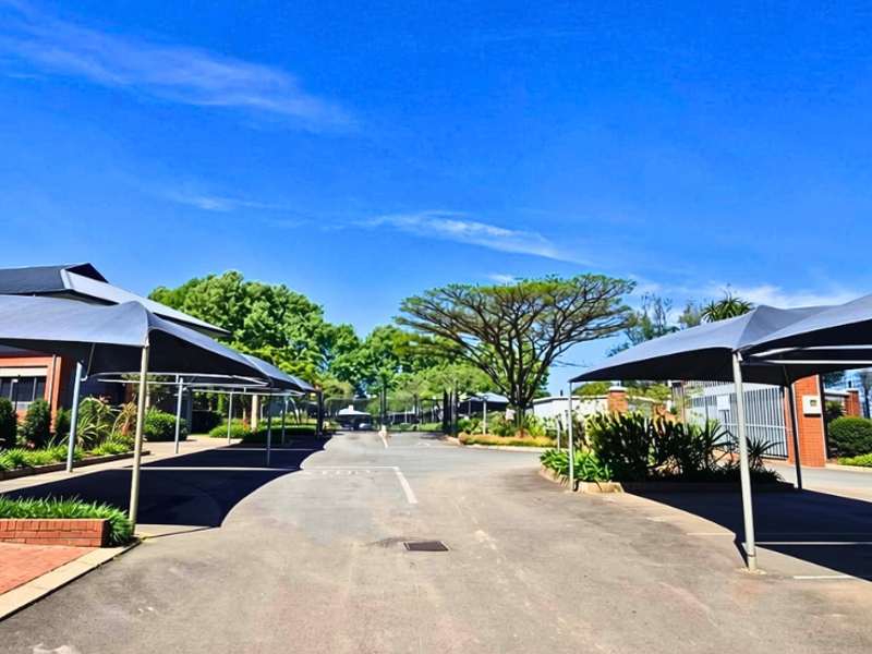 A well-maintained office property entrance featuring paved driveway access, shaded parking bays, and established landscaped garden areas.
