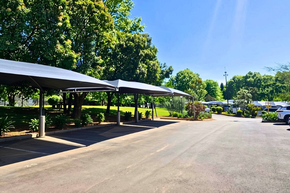 A well-maintained outdoor parking area featuring covered shade cloth carports, paved surfaces, and established surrounding greenery.