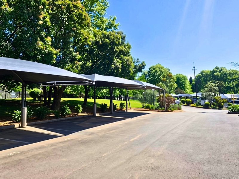 A well-maintained outdoor parking area featuring covered shade cloth carports, paved surfaces, and established surrounding greenery.