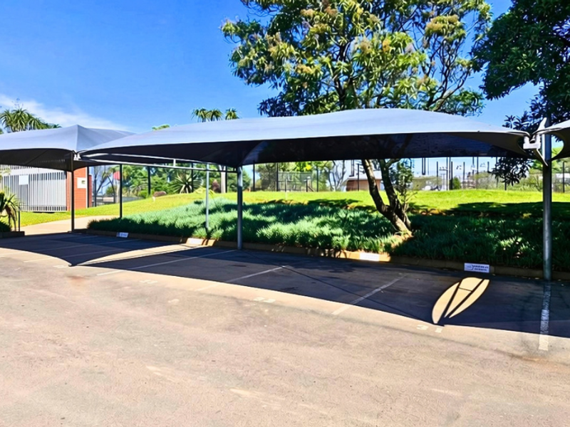 A well-maintained outdoor parking area featuring covered shade cloth carports and paved bays set within a landscaped office environment.