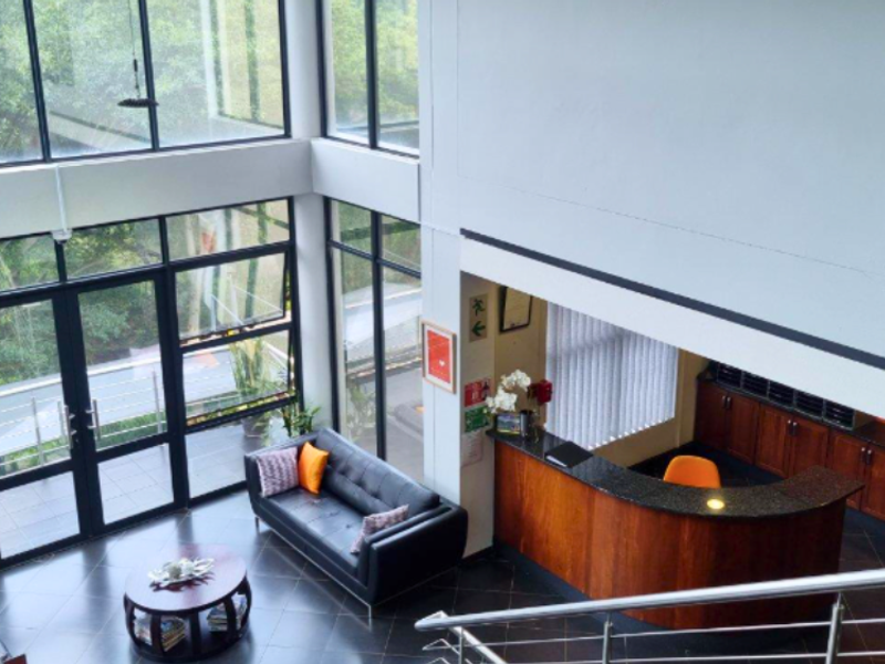 Spacious double-volume commercial entrance foyer featuring floor-to-ceiling windows, a built-in reception desk, and modern stainless steel staircase balustrades.