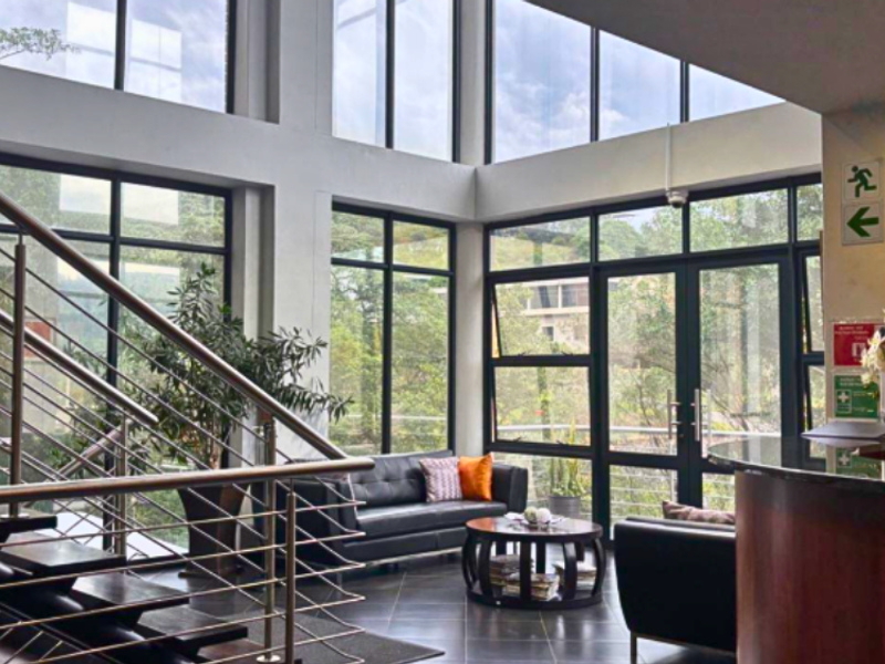 Modern commercial entrance lobby featuring double-volume windows, dark tiled flooring, and a professional reception area with a stainless steel staircase.