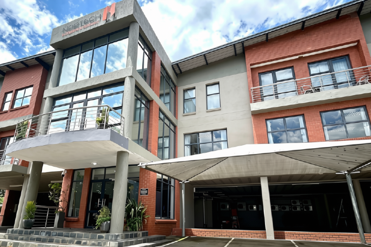 A modern multi-story commercial office building featuring a combination of brick and glass facade, balconies with steel railings, and a covered parking area.