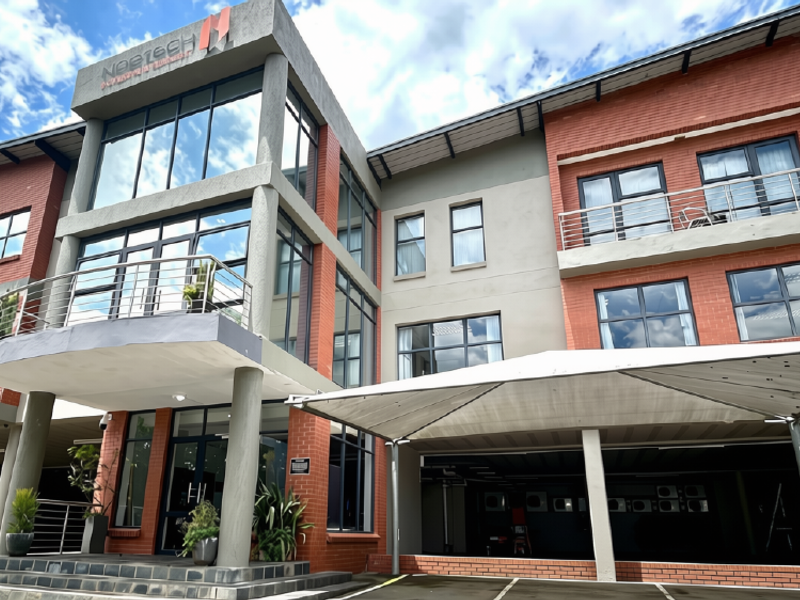 A modern multi-story commercial office building featuring a combination of brick and glass facade, balconies with steel railings, and a covered parking area.
