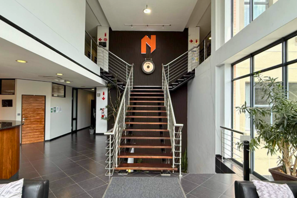 Spacious commercial entrance lobby featuring a central staircase with stainless steel balustrades, tiled flooring, and large windows providing ample natural light.