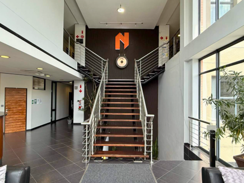 Spacious commercial entrance lobby featuring a central staircase with stainless steel balustrades, tiled flooring, and large windows providing ample natural light.