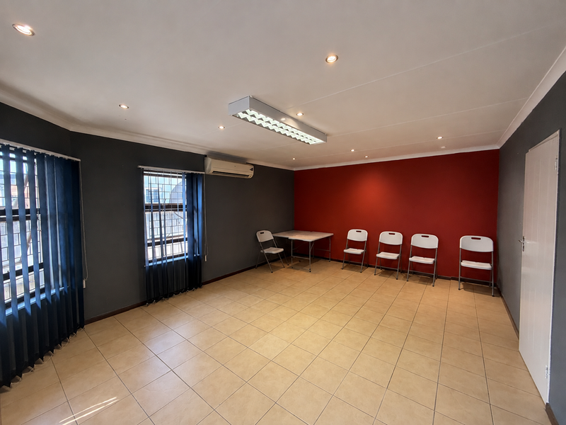 A functional office space featuring tiled flooring, recessed lighting, a split-system air conditioner, and large windows with vertical blinds and security bars.
