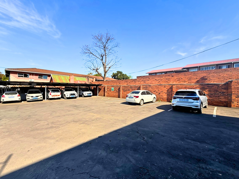 An outdoor parking area featuring an asphalt surface, covered parking bays, and a brick boundary wall.
