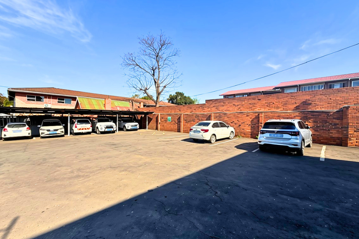 An outdoor parking area featuring an asphalt surface, covered parking bays, and a brick boundary wall.