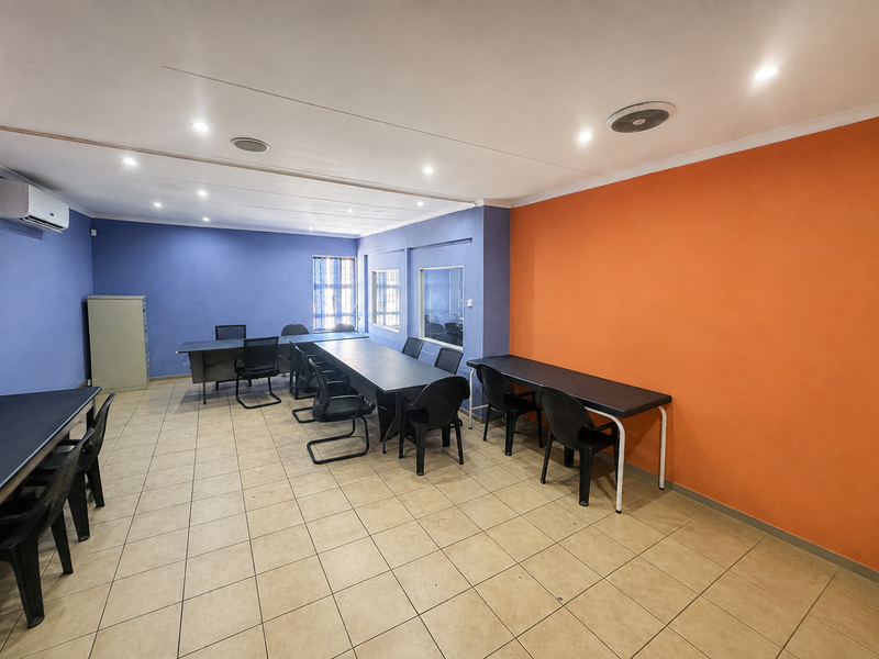 Spacious office area featuring tiled flooring, recessed lighting, air conditioning, and vibrant accent walls, suitable for a collaborative workspace or meeting room.