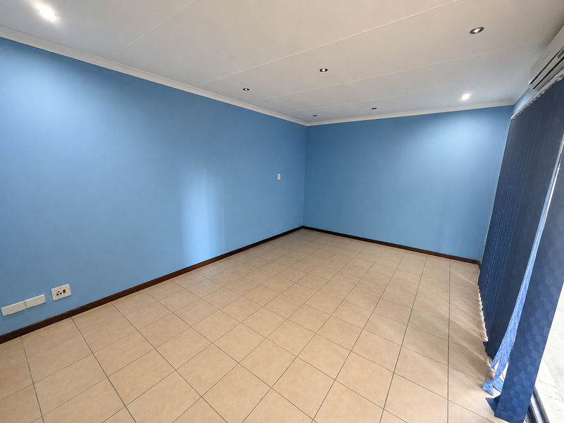 A bright, empty office space featuring neutral tiled flooring, recessed downlighting, an air conditioning unit, and blue painted walls.
