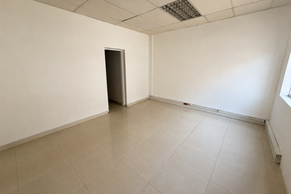 An empty commercial office space featuring ceramic floor tiles, a suspended ceiling with recessed lighting, and neutral white walls.