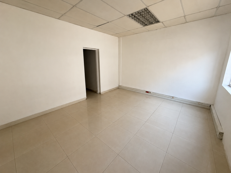 An empty commercial office space featuring ceramic floor tiles, a suspended ceiling with recessed lighting, and neutral white walls.