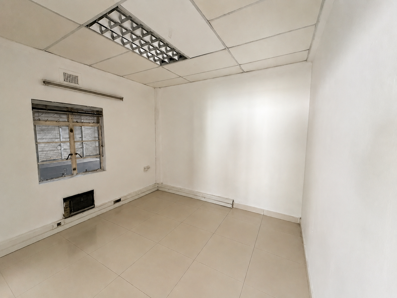 A vacant commercial office space featuring tiled flooring, a suspended ceiling with recessed lighting, and a built-in air conditioning unit.