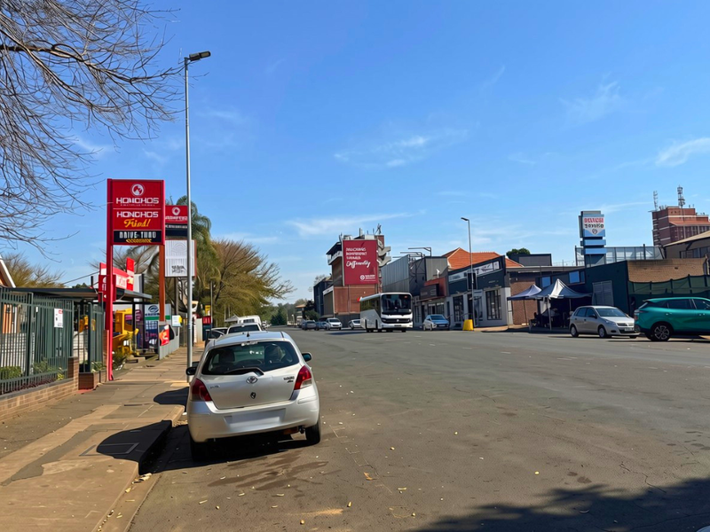 A street-level view of a commercial area featuring paved sidewalks, street lighting, and various commercial signage along the roadside.