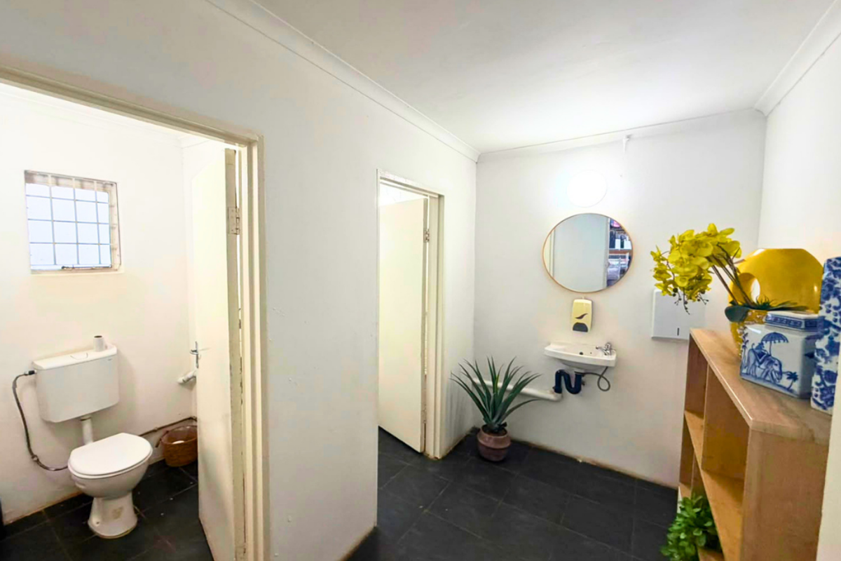 A functional commercial restroom featuring a wall-mounted basin, toilet, and dark tiled flooring with neutral white walls.