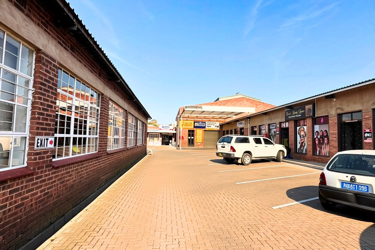 A view of a commercial property courtyard featuring a paved parking area, brick building facades, and multiple storefront entrances.