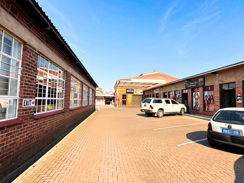 A view of a commercial property courtyard featuring a paved parking area, brick building facades, and multiple storefront entrances.