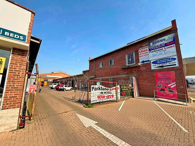 Front exterior view of a commercial property featuring brick facade, paved parking area, and multiple business signs.