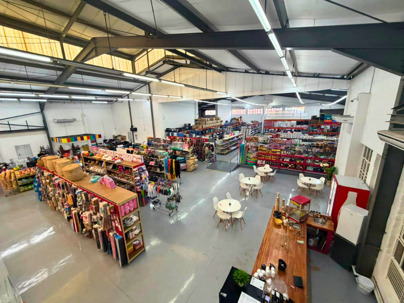 Spacious commercial open-plan retail area featuring high exposed steel trusses, industrial epoxy flooring, ample natural light from skylights, and a functional service counter.