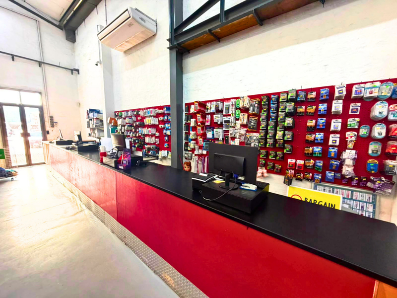 Commercial retail space featuring a long built-in service counter, extensive wall-mounted display pegboards, exposed structural steel beams, and high ceilings with air conditioning.