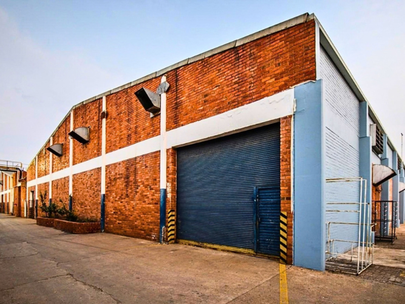 Industrial warehouse exterior featuring a large roller shutter door, brick facade, and external ventilation units, situated on a concrete driveway.