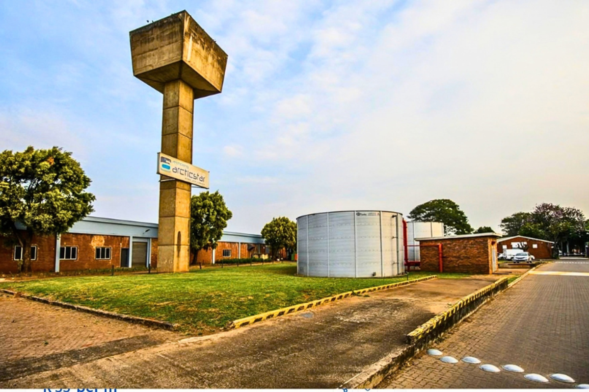 Industrial property exterior featuring a prominent water tower, large storage tanks, and paved access areas with brick building facades.