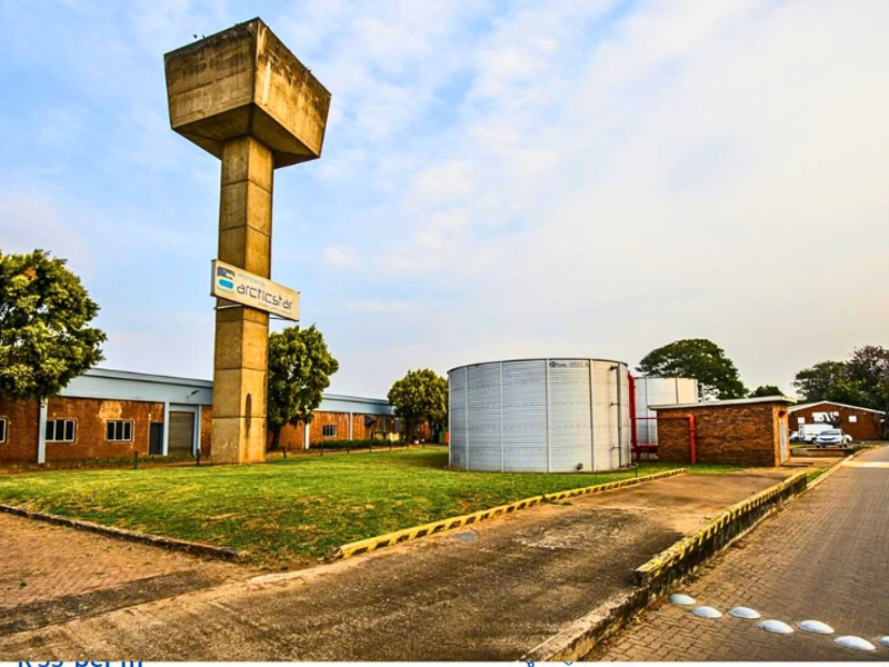 Industrial property exterior featuring a prominent water tower, large storage tanks, and paved access areas with brick building facades.