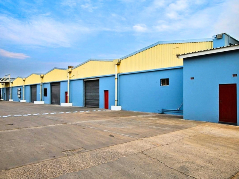 Industrial warehouse complex featuring multiple roller shutter doors, concrete yard space, and durable metal cladding exterior.