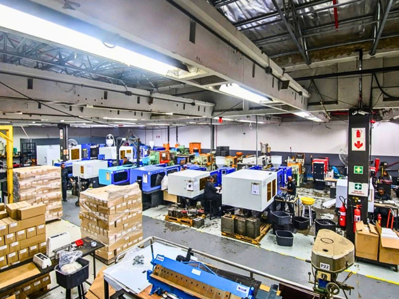 Spacious industrial manufacturing facility featuring high ceilings with exposed steel trusses, fluorescent lighting, and durable concrete flooring suitable for heavy-duty operations.