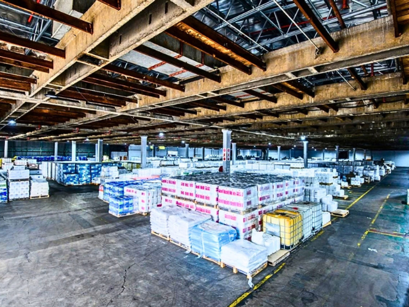 Large industrial warehouse space featuring high ceilings with exposed concrete beams, fire sprinkler infrastructure, and durable concrete flooring.