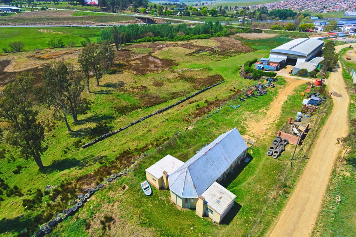 Aerial view of a commercial property featuring a main building, a large warehouse structure, and extensive surrounding land with dirt access roads.