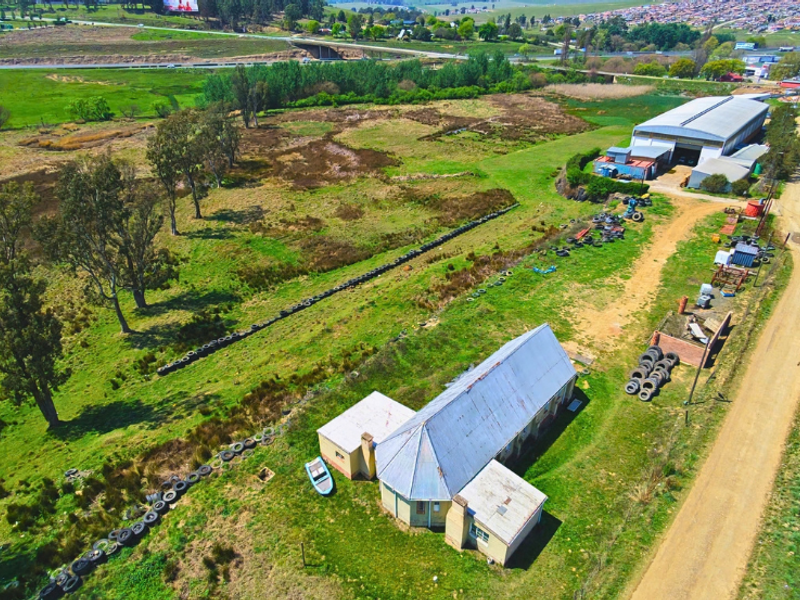 Aerial view of a commercial property featuring a main building, a large warehouse structure, and extensive surrounding land with dirt access roads.