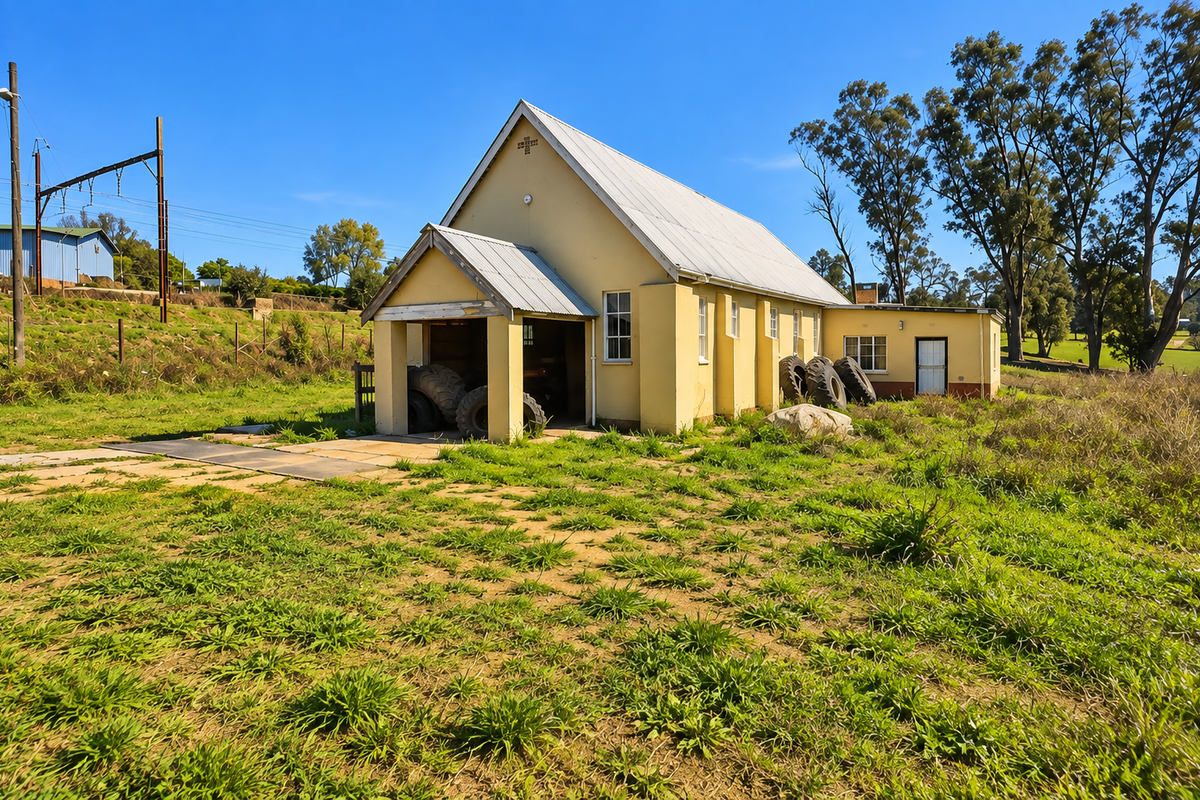 A detached commercial building featuring a metal roof and stucco exterior, situated on a large plot with surrounding grass and mature trees.