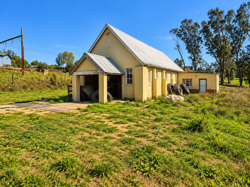A detached commercial building featuring a metal roof and stucco exterior, situated on a large plot with surrounding grass and mature trees.